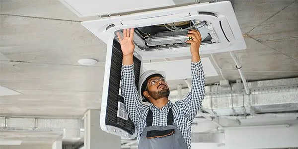 Technician maintaining a ceiling-mounted HVAC unit